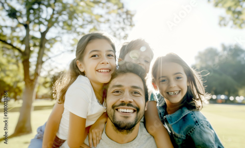 A happy family portrait featuring parents and their two young daughters smiling warmly while sitting together on a couch. photo