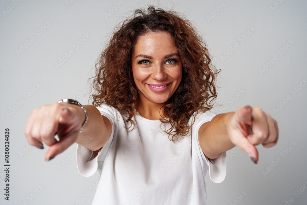 A young woman with curly hair playfully points towards the camera in a bright studio A young woman with curly hair playfully points towards the camera in a bright studio