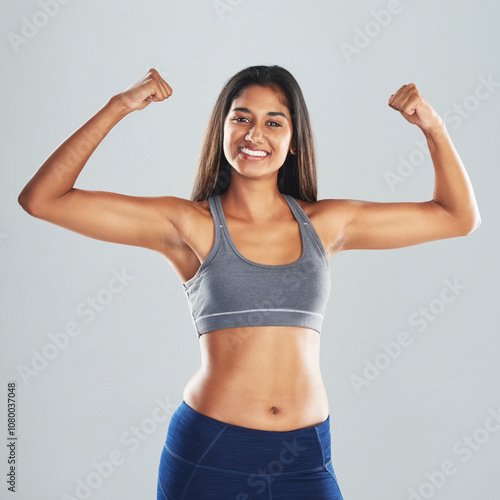 Fitness, portrait and girl flexing arms in studio with smile, confidence and healthy gym champion. Power, muscle and strong Indian woman athlete with happy face, pride or wellness on grey background photo