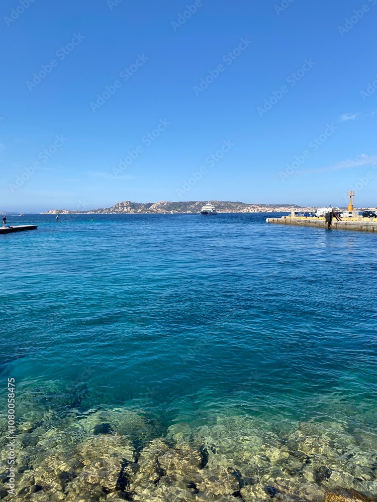 Crystal clear turquoise waters near La Maddalena, Sardinia, with gentle waves lapping over rocky seabed, under an expansive blue sky showcasing the island's coastal allure.
Crystal clear turquoise waters near La Maddalena, Sardinia, with gentle waves lapping over rocky seabed, under an expansive blue sky showcasing the island's coastal allure.
