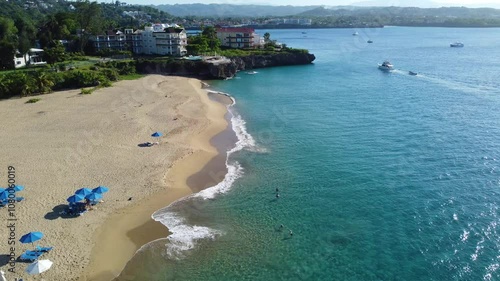 A 4k drone shot of Playa Alicia in Sosua, Dominican Republic. People are swimming and enjoying the beach on a beautiful day in the Caribbean. photo