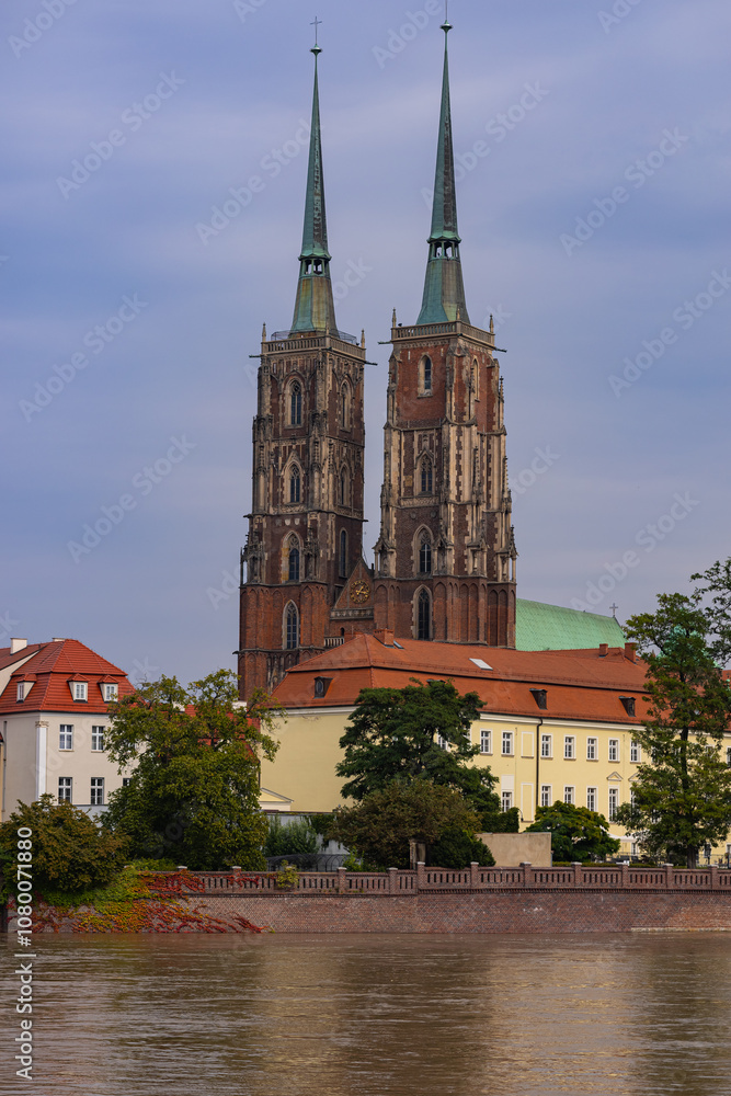 Naklejka premium Historic twin-spired cathedral in Wroclaw with rising river water levels after heavy rainfall on a cloudy day. Concept of climate impact and environmental awareness