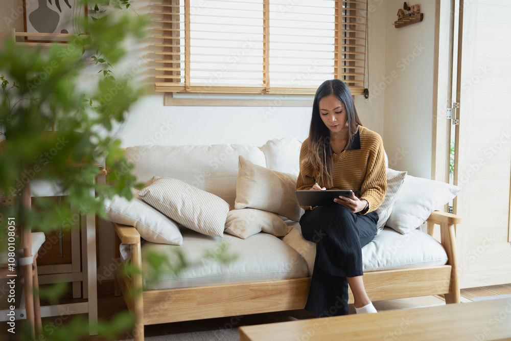 Obraz premium Peaceful millennial woman working with digital tablet in a minimalist living room