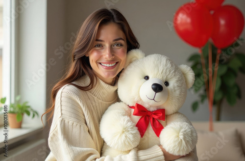 Young smiling brunette woman holding big teddy bear in bright modern living room decorated for Valentine's Day. Romantic gift for February 14