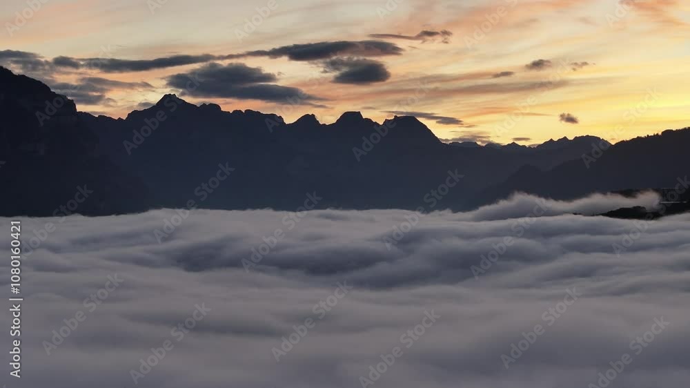 Aerial view of Lake Walensee in Switzerland, blanketed in a thick layer of fog and clouds, with mountain peaks emerging as silhouettes against the dawn sky. Aerial view of Lake Walensee in Switzerland, blanketed in a thick layer of fog and clouds, with mountain peaks emerging as silhouettes against the dawn sky.