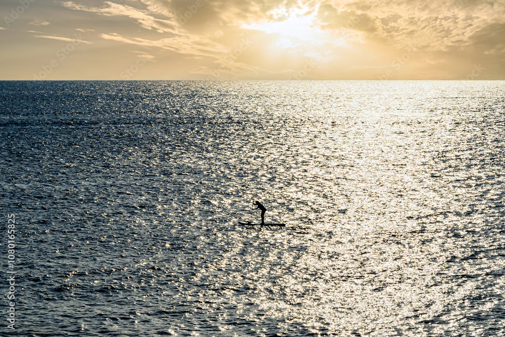 Fototapeta premium Silhouette of a woman practicing paddle surfing in the sea of ​​Menorca at sunset. Balearic Islands