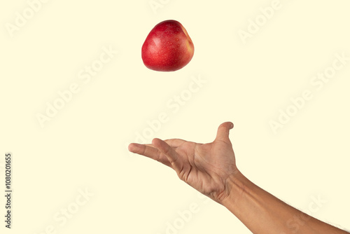 Male hand tossing a red apple in the air isolated on yellow background photo