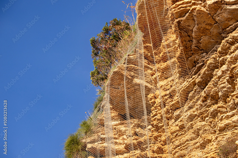 Obraz premium Protective netting securing a cliff face from rockfalls under blue sky