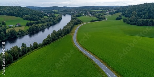 A stunning aerial view of a winding road through lush green fields and a serene river under a vast, open sky.