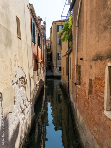 A narrow canal in Venice, Italy, reflecting the colorful facades of historic buildings. The calm water mirrors the architecture, creating a serene and picturesque scene.  photo