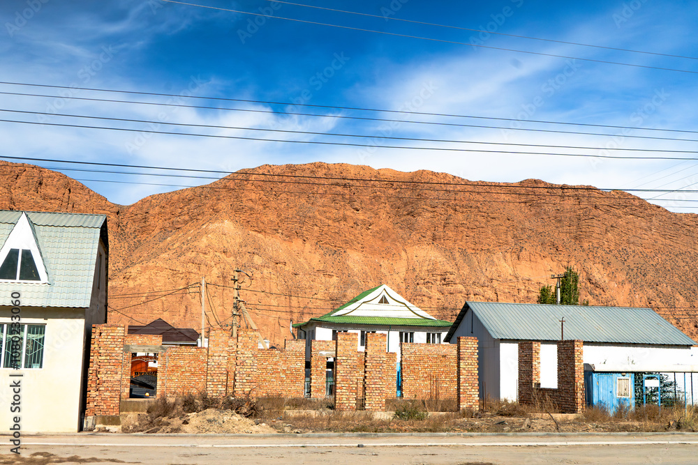 Rural residential area set against a rocky mountain backdrop, with brick fences, homes, and utility lines cutting across the landscape. Depicts the contrast of man-made structures and rugged nature Rural residential area set against a rocky mountain backdrop, with brick fences, homes, and utility lines cutting across the landscape. Depicts the contrast of man-made structures and rugged nature