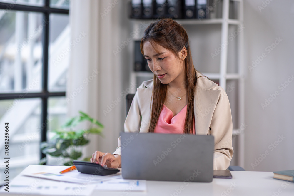 Asian Business woman using calculator and laptop for doing math finance on an office desk, tax, report, accounting, statistics, and analytical research concept Asian Business woman using calculator and laptop for doing math finance on an office desk, tax, report, accounting, statistics, and analytical research concept