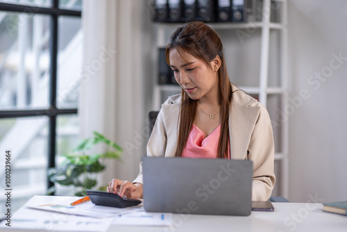 Asian Business woman using calculator and laptop for doing math finance on an office desk, tax, report, accounting, statistics, and analytical research concept 