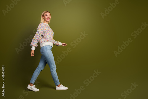 Confident young woman in colorful knit sweater walking against khaki background, showcasing fashion and style concepts in casual jeans and sneakers photo