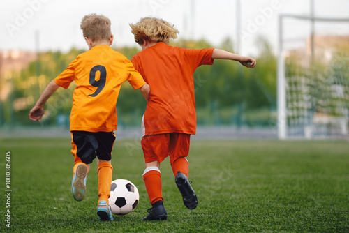 Happy Children Play Soccer Ball on Grass Pitch. Kids in Red and Orange Football Teams in Match. Boys Soccer Teams Competing For The Ball During A Football Match. Kids Play Sports In the Stadium