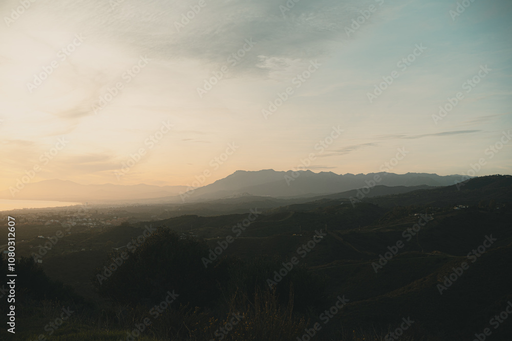 Softly lit hills and distant mountains under a golden sunset, creating a peaceful natural landscape Softly lit hills and distant mountains under a golden sunset, creating a peaceful natural landscape