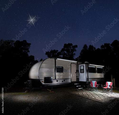 Obraz na płótnie Christmas star high in the night sky above a travel trailer campsite with trees from a forest silhouetted behind. w salonie