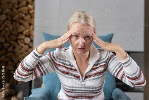 Foto Middle-aged woman indoors with a concentrated expression, massaging her temples in a casual home environment