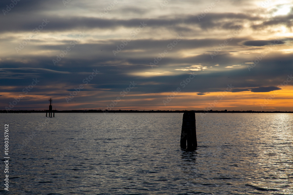 A quiet red sunset over the lagoon, with the Venetian bricole (limit of the navigable canal) backlit on the sea, Chioggia, Venice area, Italy A quiet red sunset over the lagoon, with the Venetian bricole (limit of the navigable canal) backlit on the sea, Chioggia, Venice area, Italy