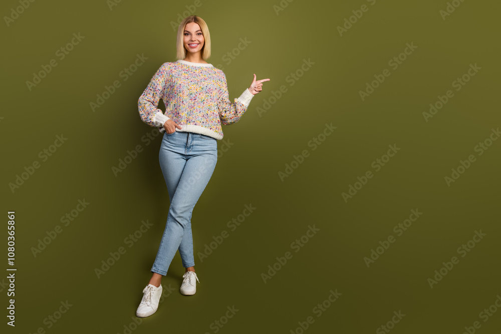 Charming young woman in colorful sweater points with smile against khaki background, showcasing casual fashion style for promotion or advertisement Charming young woman in colorful sweater points with smile against khaki background, showcasing casual fashion style for promotion or advertisement