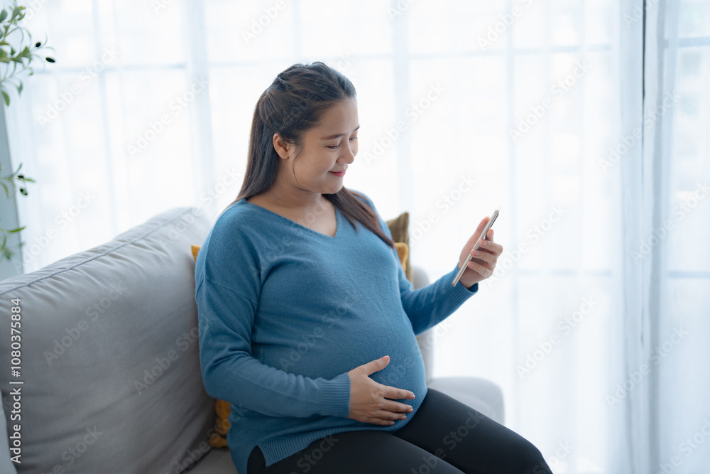 Pregnant asian woman holding smartphone at home using mobile app for pregnant women Positive life moment in pregnancy time Pregnant asian woman holding smartphone at home using mobile app for pregnant women Positive life moment in pregnancy time
