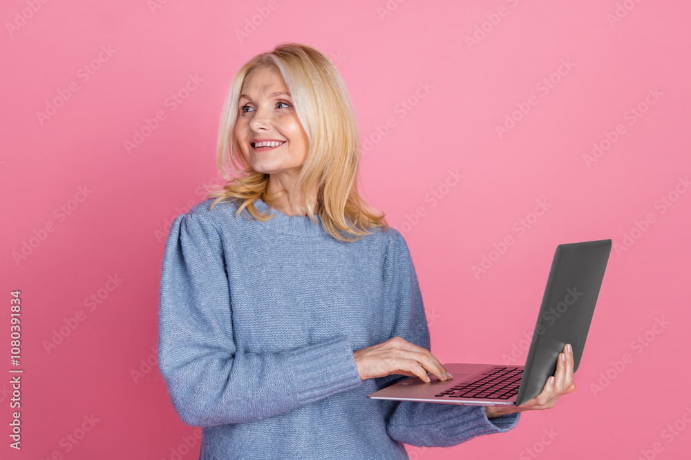 Photo of attractive senior woman hold netbook look empty space dressed stylish blue knitted clothes isolated on pink color background Photo of attractive senior woman hold netbook look empty space dressed stylish blue knitted clothes isolated on pink color background