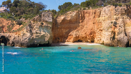 A couple paddles together on a stand-up board in Algarve’s blue ocean near scenic cliffs