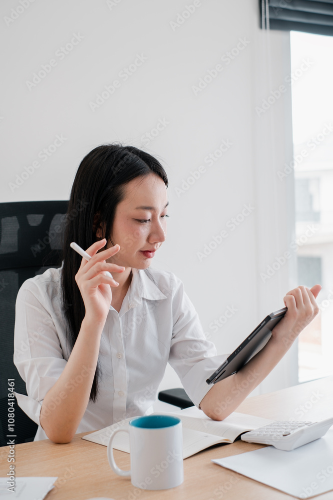 Professional woman in white shirt using tablet at work desk with coffee mug and calculator, focused on digital analysis. Professional woman in white shirt using tablet at work desk with coffee mug and calculator, focused on digital analysis.
