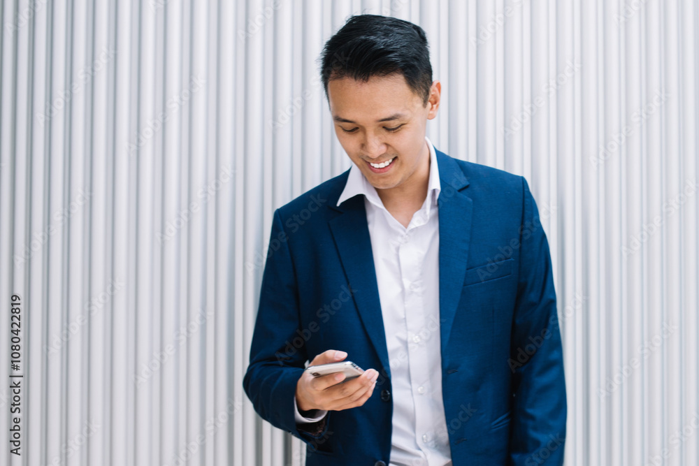 Positive stylish modern Asian businessman standing and browsing on smartphone