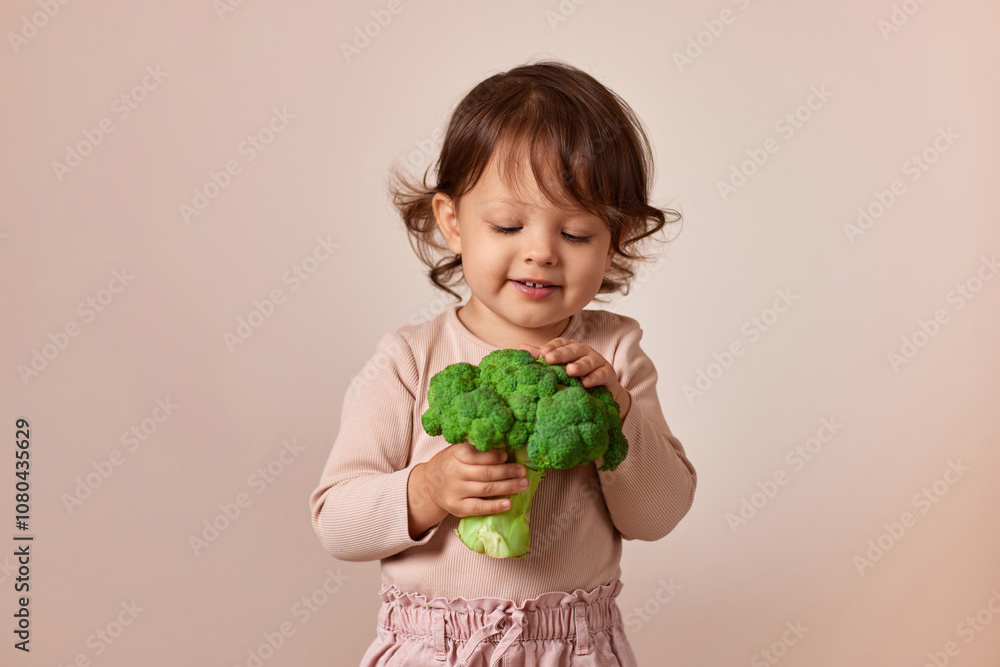 happy child girl holding fresh green raw broccoli on beige background. healthy baby food. kid loves vegetables happy child girl holding fresh green raw broccoli on beige background. healthy baby food. kid loves vegetables