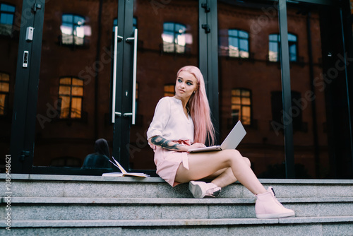 Pinked haired woman looking away working on laptop on stairs outside photo