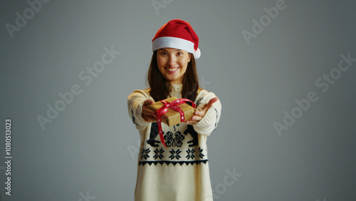 Fun cute woman hold small Christmas gift on gray isolated studio background. Joyful girl give new year eve present. Person wear red Santa Claus hat receive packaging box. Winter holiday xmas surprise.