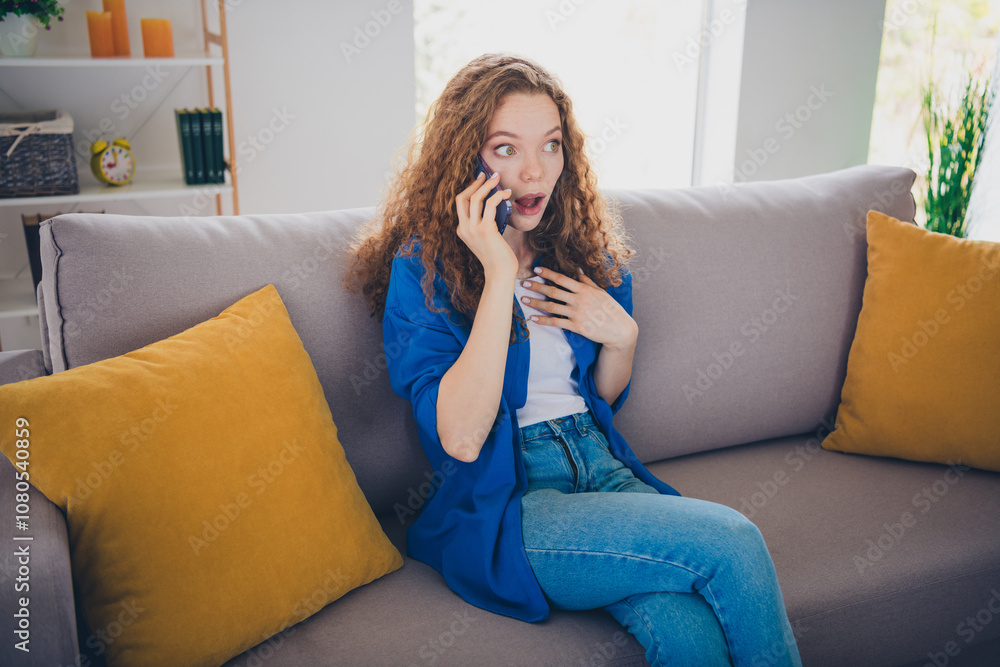 Photo of shocked charming girl wear blue shirt sit divan speak phone day weekend living room apartment flat indoors