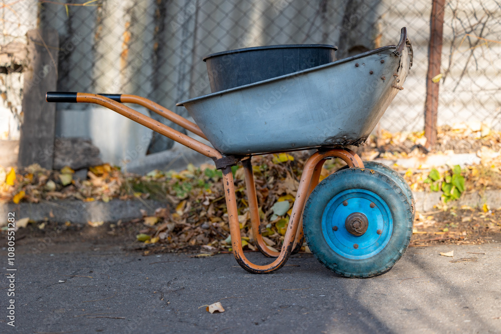 An old metal wheelbarrow with blue wheels in the garden An old metal wheelbarrow with blue wheels in the garden