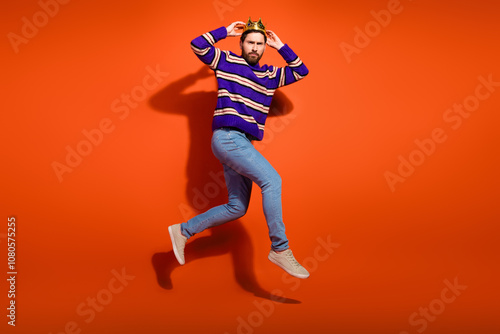 Full length photo of handsome young guy touch crown running jump dressed stylish striped purple garment isolated on orange color background