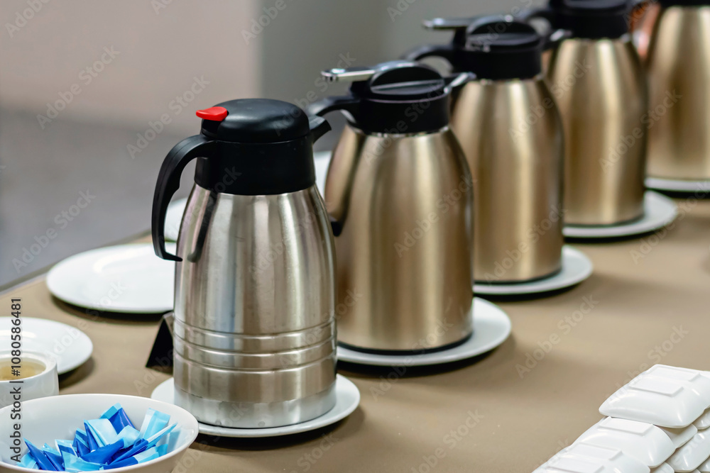 Row of many kettles, milk bottle and stack of white ceramic dish ready for party. Dishware on table for buffet. Many pitcher or kettle in restaurant. Self-service breakfast. Selective focus.