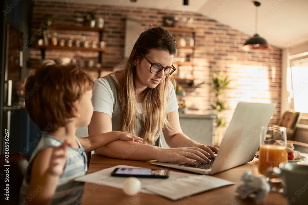 Mother working from home with young son by her side at kitchen table Mother working from home with young son by her side at kitchen table