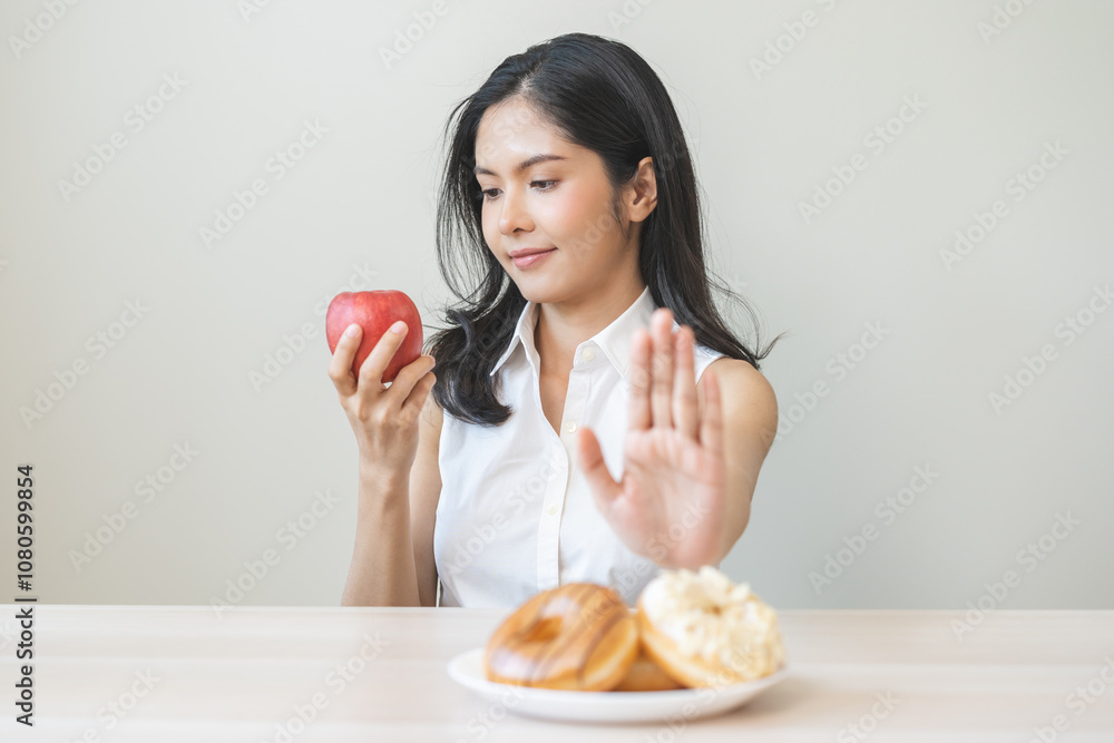 Diet asian young woman hand push out, refuse sugar donut, doughnut and sweet taste on plate and choose red apple for good health, fighting to keep it from getting fat. Healthy nutrition of weight loss Diet asian young woman hand push out, refuse sugar donut, doughnut and sweet taste on plate and choose red apple for good health, fighting to keep it from getting fat. Healthy nutrition of weight loss