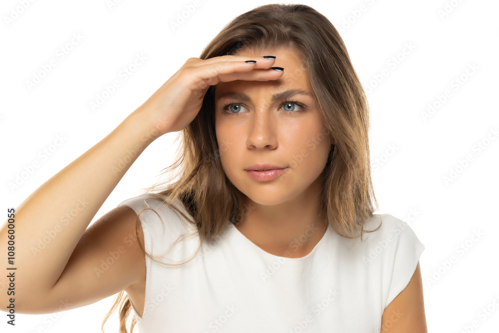Curious brunette woman in white shirt looking far away with hand over head, trying to see something Curious brunette woman in white shirt looking far away with hand over head, trying to see something