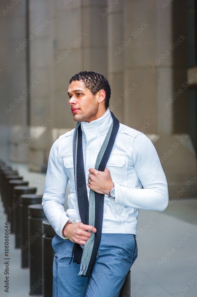 A man stands outside in front of a modern building, wearing a light jacket and a scarf. He appears relaxed and confident, holding the scarf with one hand while looking into the distance.