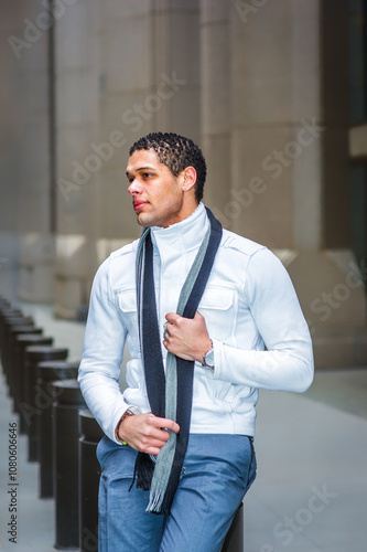 Obraz na płótnie A man stands outside in front of a modern building, wearing a light jacket and a scarf. He appears relaxed and confident, holding the scarf with one hand while looking into the distance. w salonie