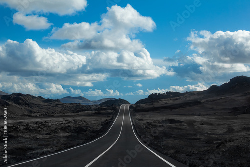 An empty asphalt road stretches through the barren volcanic landscape of Timanfaya National Park in Lanzarote, Canary Islands, Spain.