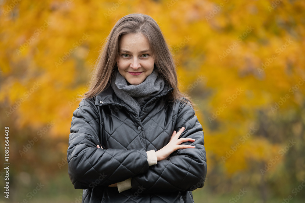 A young woman stands with her arms crossed, smiling warmly while surrounded by bright yellow and orange leaves in a peaceful outdoor environment during autumn. A young woman stands with her arms crossed, smiling warmly while surrounded by bright yellow and orange leaves in a peaceful outdoor environment during autumn.