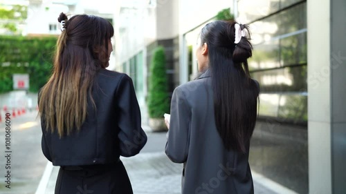 Two young Asian businesswomen outside their company with a skyscraper in the background.