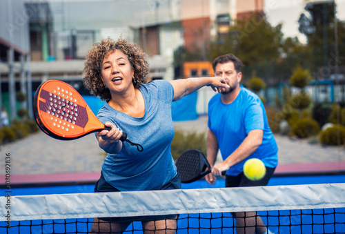 Mixed adult couple palying padel on outdoor court.