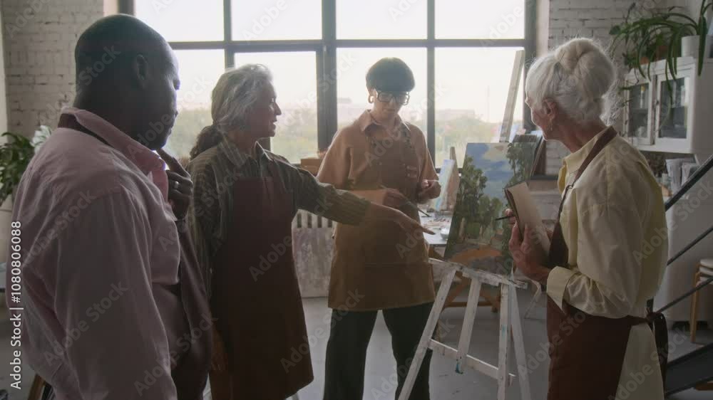 Group of two senior women and man standing near painting placed on easel discussing result with young female teacher in art class Group of two senior women and man standing near painting placed on easel discussing result with young female teacher in art class