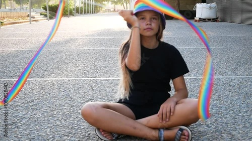 A young girl holds a rainbow lgbtq ribbon, embodying childhood joy