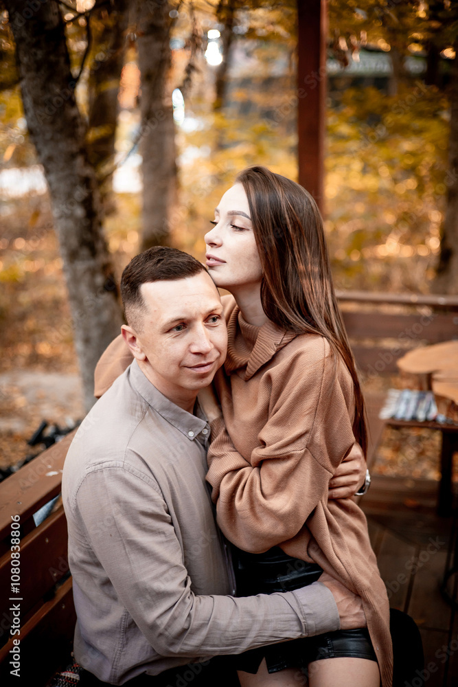 a young couple guy with a girl in autumn in a cafe in brown and orange tones on an outdoor terrace hugging and kissing, love or Valentine's day a young couple guy with a girl in autumn in a cafe in brown and orange tones on an outdoor terrace hugging and kissing, love or Valentine's day