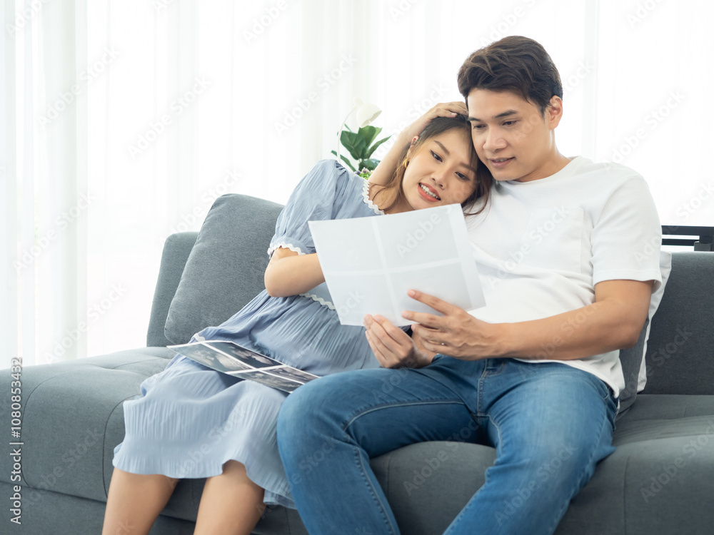 A happy Asian couple. Handsome husband and his beautiful wife pregnant and hold ultrasound picture of baby at home. A happy Asian couple. Handsome husband and his beautiful wife pregnant and hold ultrasound picture of baby at home.