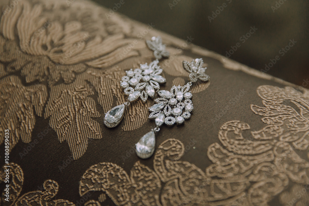 Obraz premium A pair of earrings with a flower design are displayed on a brown cloth. The earrings are made of crystal and have a drop-shaped design. The cloth is a brown color and has a floral pattern